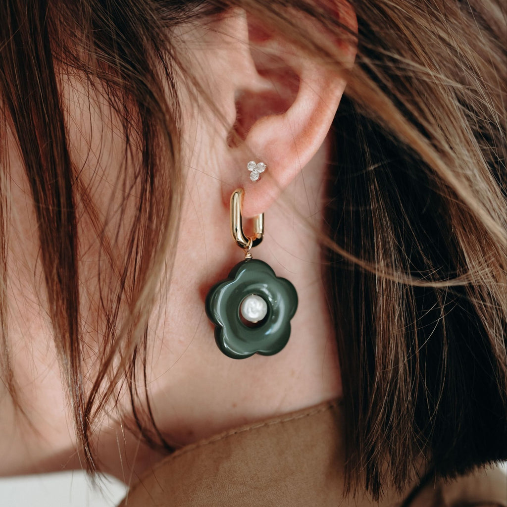 Close-up of an ear wearing a green floral earring with a pearl center.