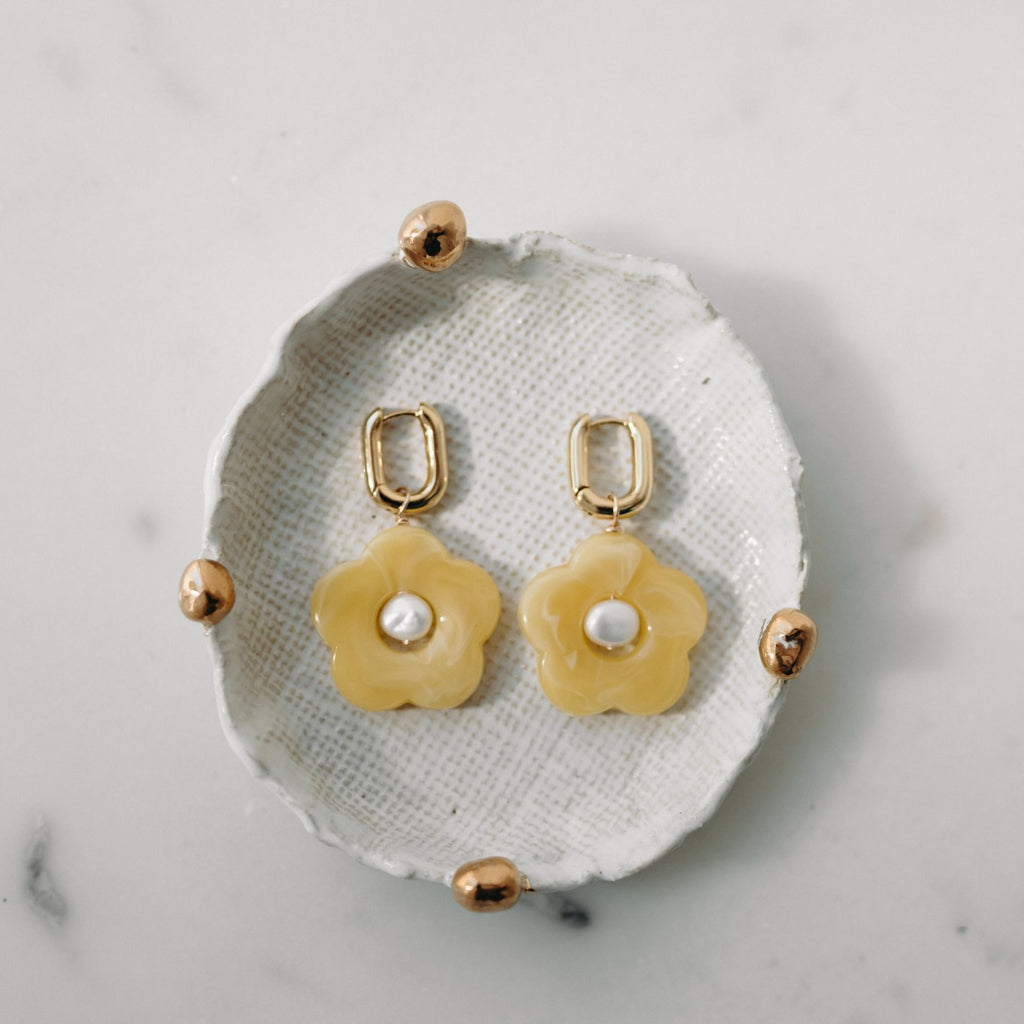 Gold and beige floral earrings on a textured white surface