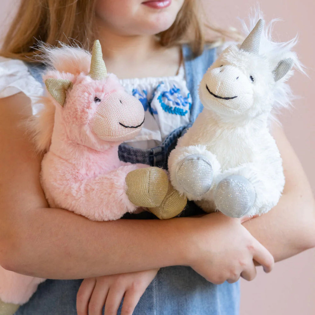 A pink and a white Glimmer Glitter Unicorn soft toy with a unicorn horn and hooves,held in a persons arms