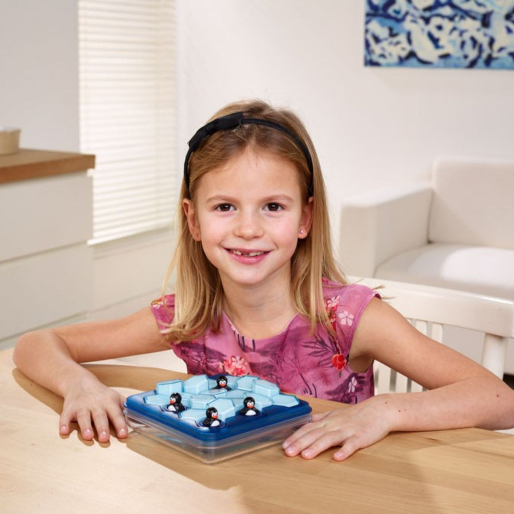Young girl playing with a penguin ice cube toy at a table.