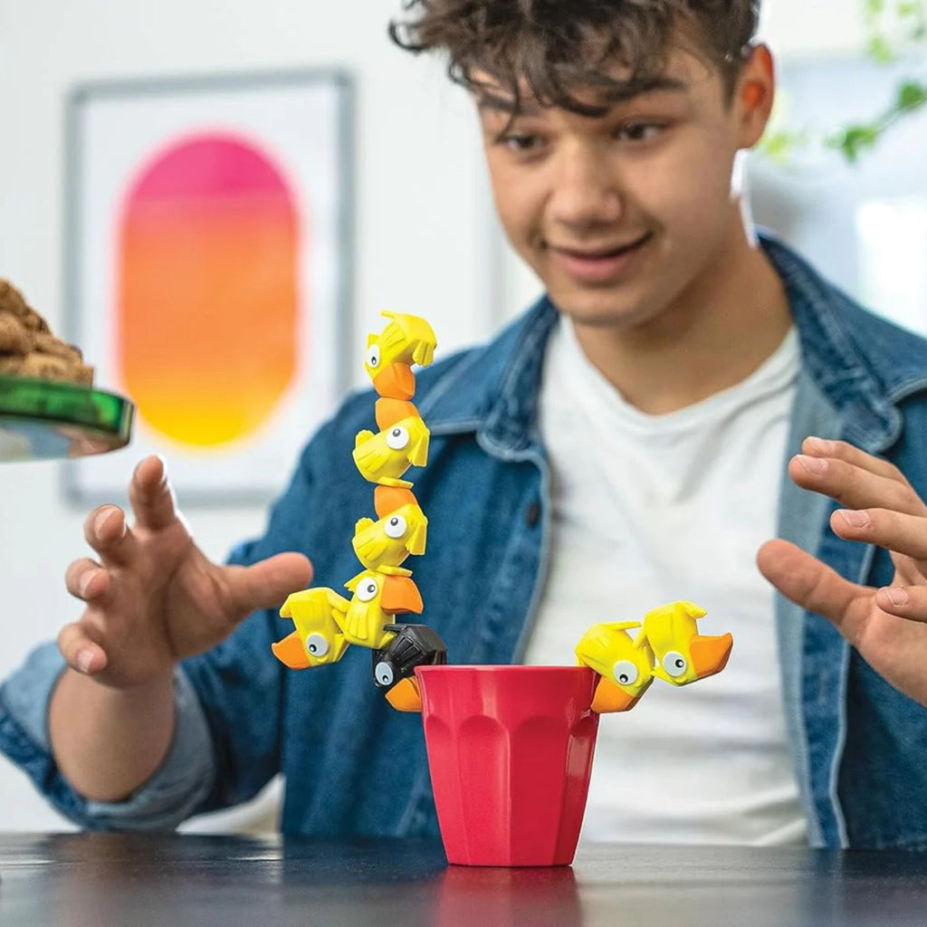 Person playing with a toy involving small yellow creatures and a red container.