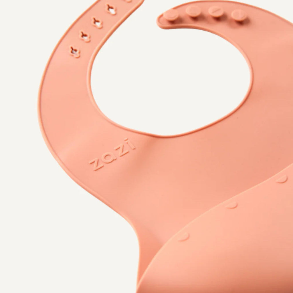 Peach-colored silicone bib with 'zazi' branding on a white background