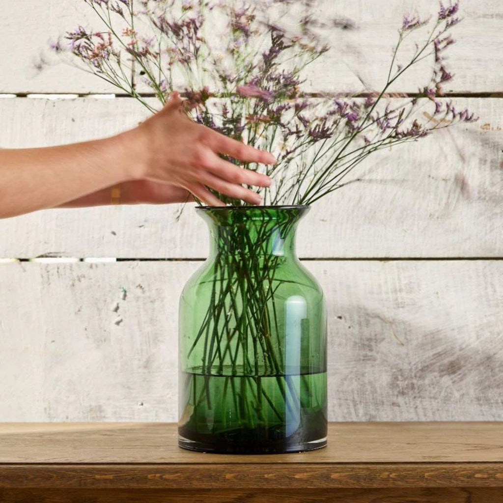 Green vase with dried flowers on a wooden surface against a wooden background