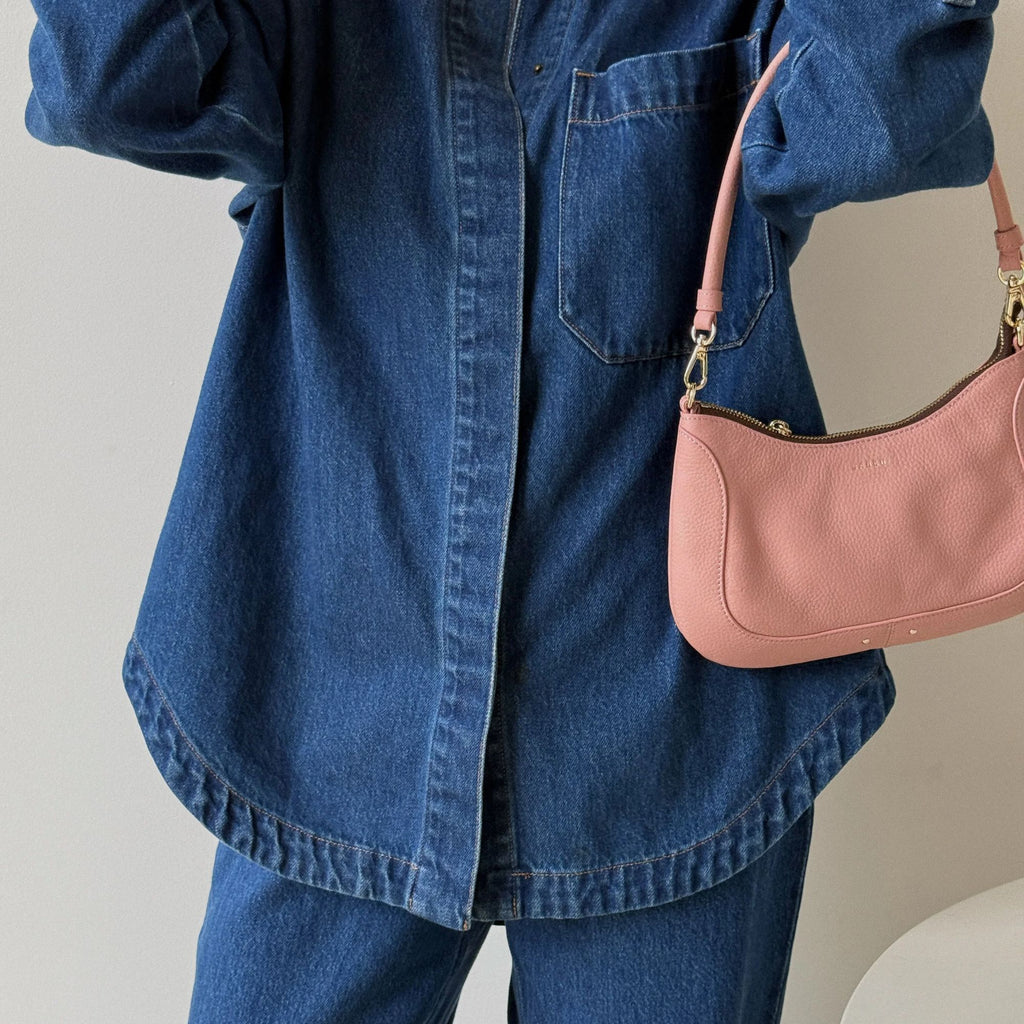 Person wearing a blue denim jacket holding a pink handbag against a neutral background