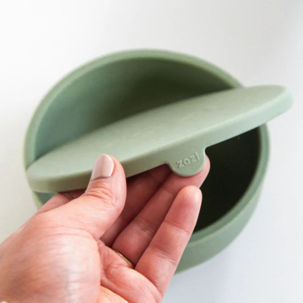 Hand holding a green silicone lid with 'zazi' branding on a white background