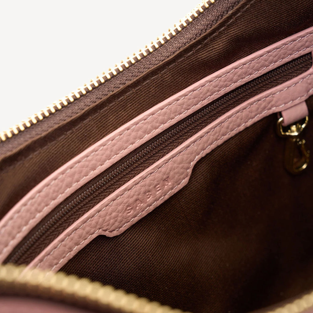 Close-up of a brown leather bag with pink interior and gold zipper.