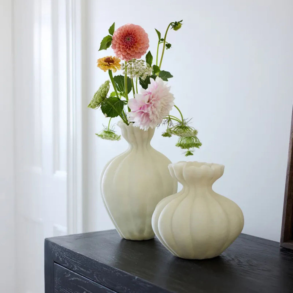 Two white vases with flowers on a dark surface against a light background