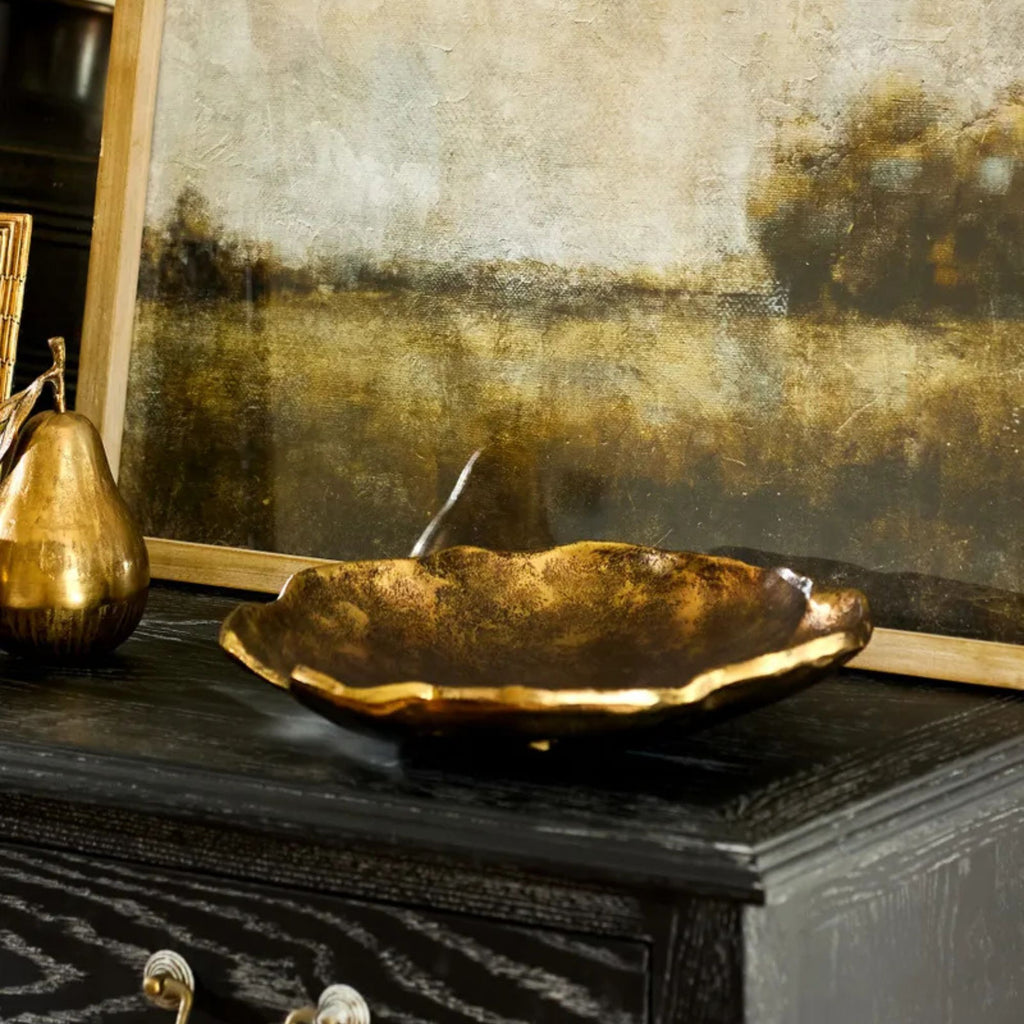 Decorative gold bowl on a dark surface with a textured wall in the background