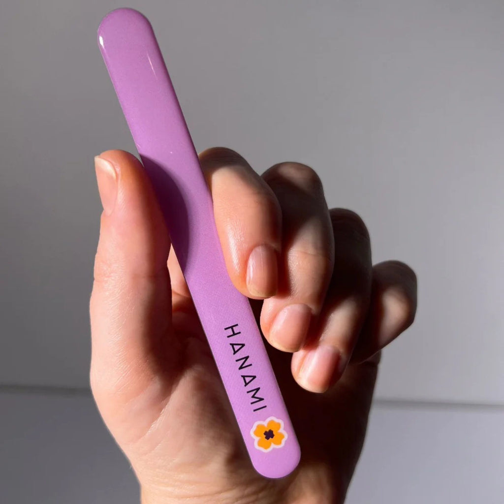 Hand holding a purple nail file with 'HANAMI' branding against a neutral background