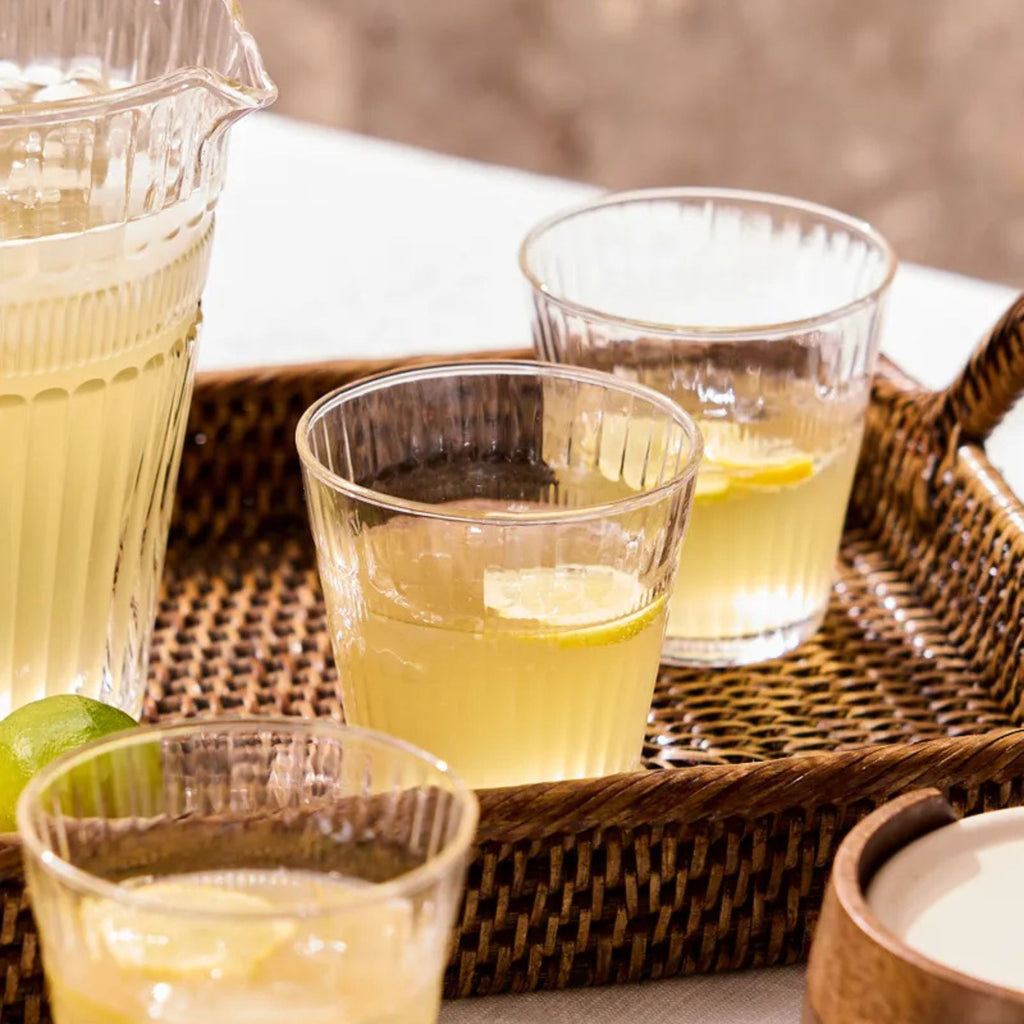 Clear glasses filled with a yellow liquid on a woven tray with a blurred background