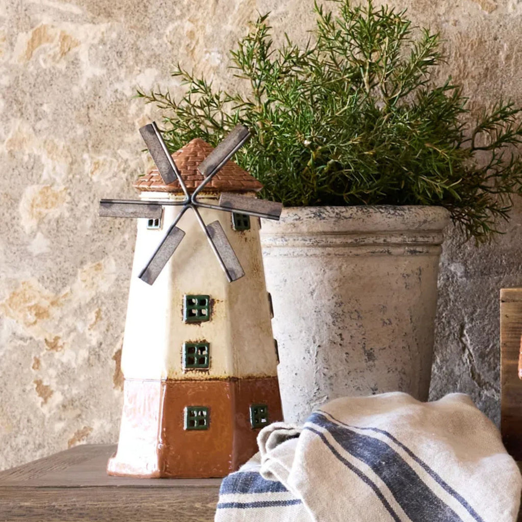 Decorative windmill with a plant  against a textured wall.
