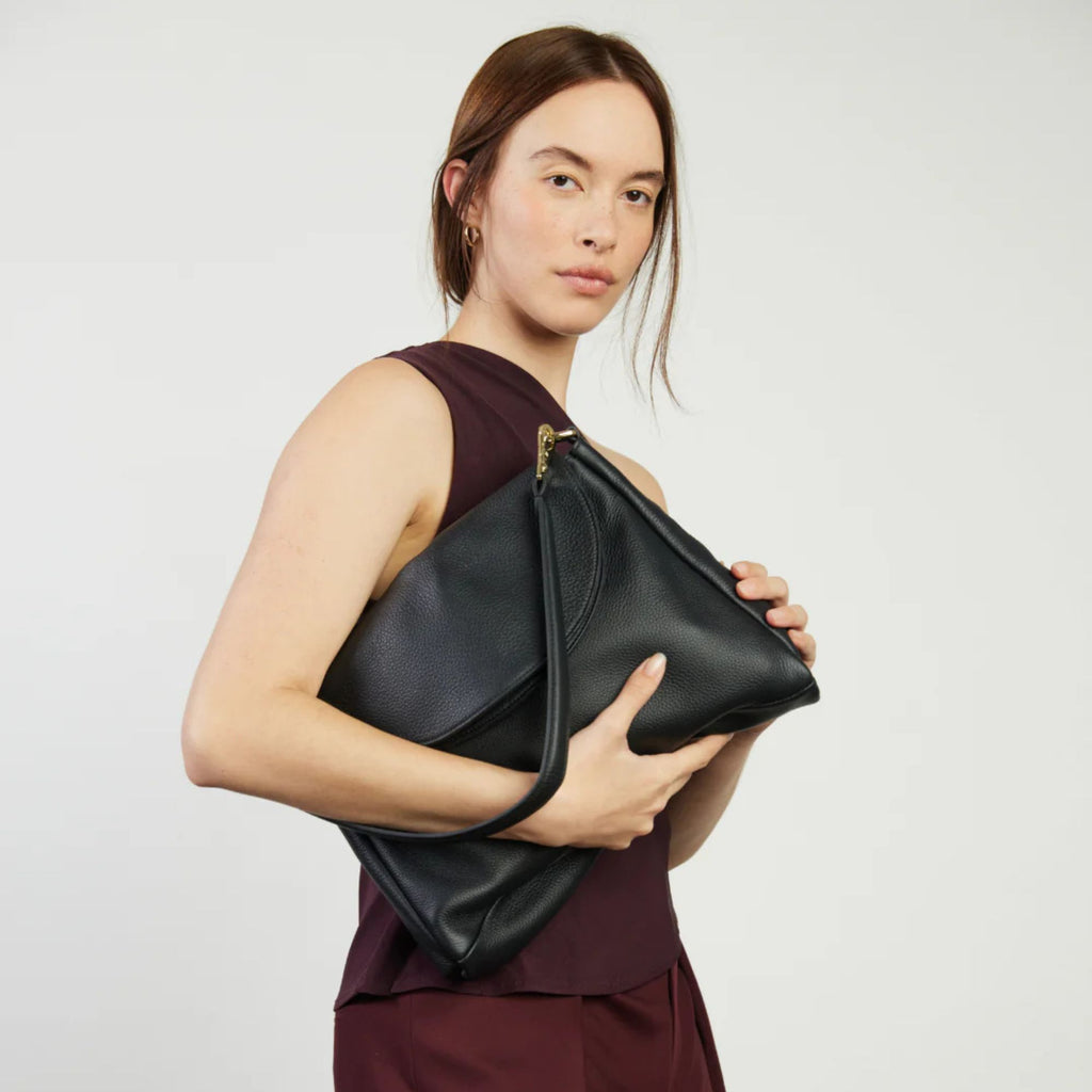 Woman holding a black leather clutch bag against a plain background