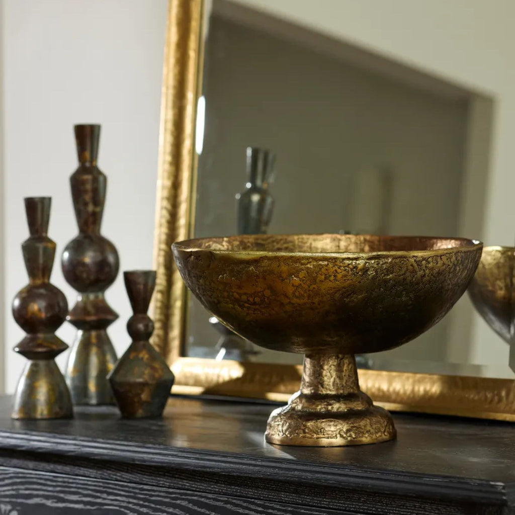 Decorative gold bowl on a dark surface with a mirror and other decorative items in the background.
