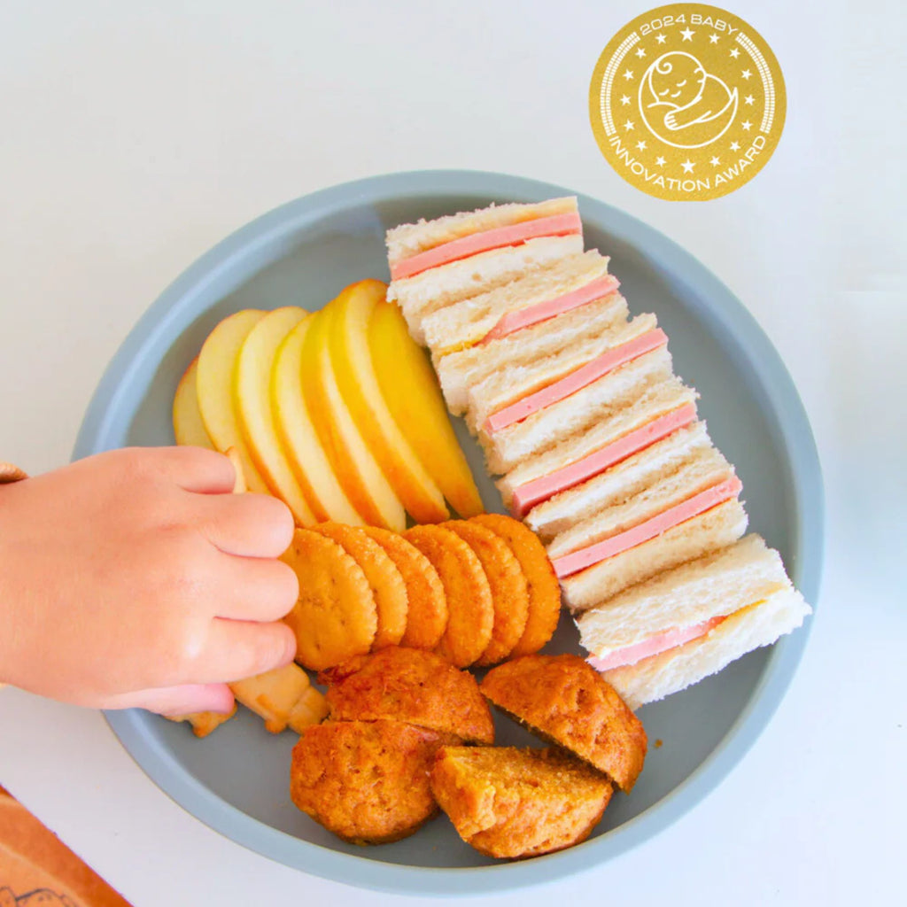 Children's lunch with sandwich, fruit, and cookies on a plate, featuring a gold badge in the corner.