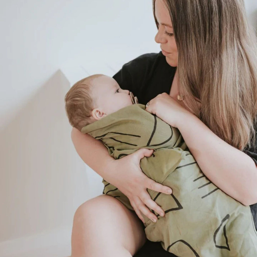 Woman holding a baby wrapped in a green blanket with black patterns on a white background