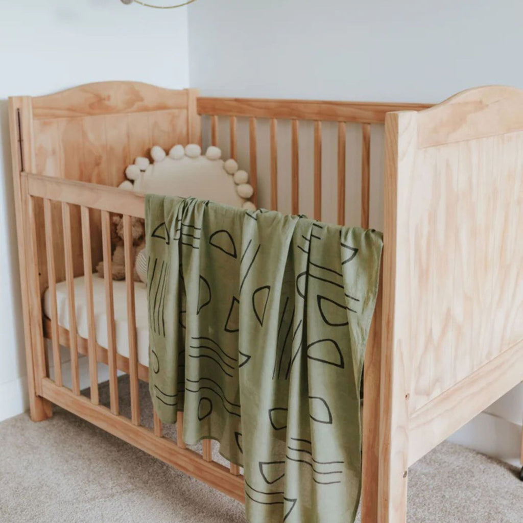Wooden crib with a green blanket featuring black abstract patterns in a nursery setting.