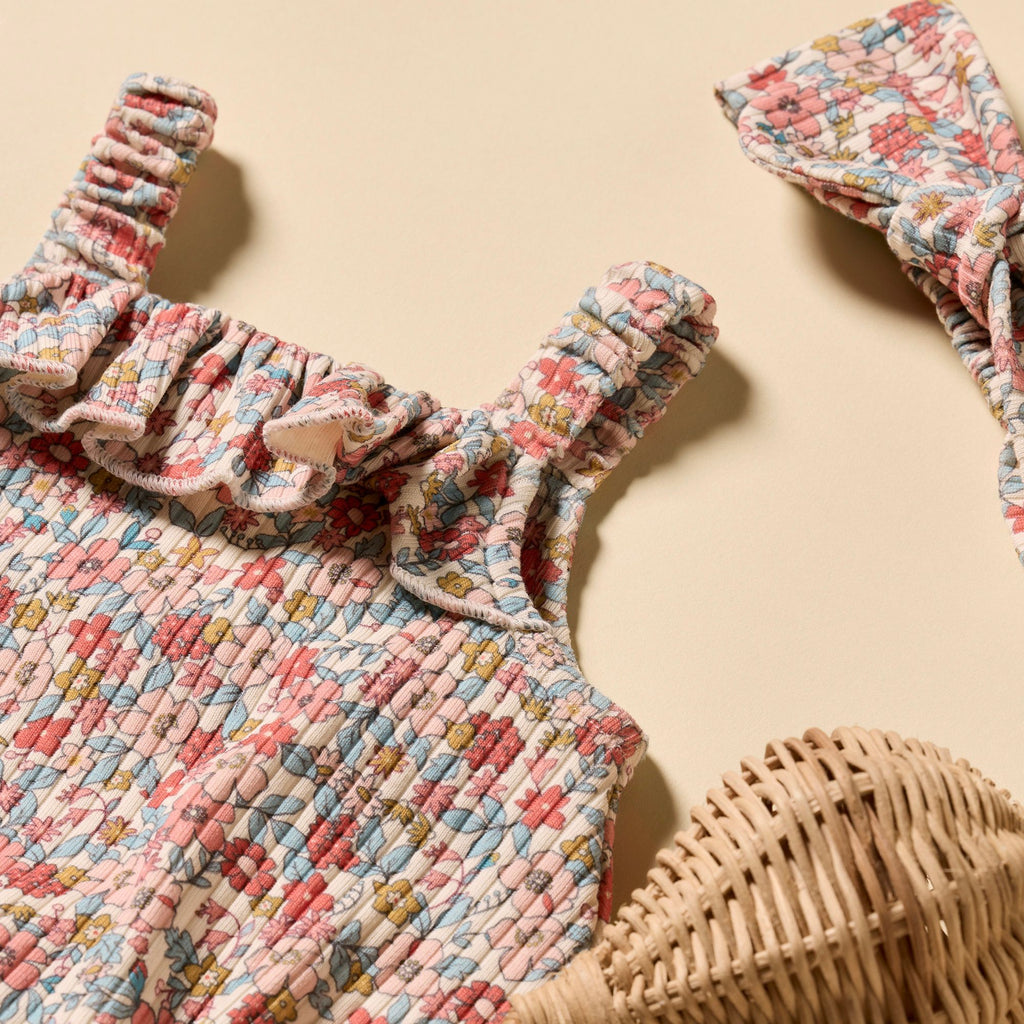 Floral patterned baby romper with ruffled straps on a beige background