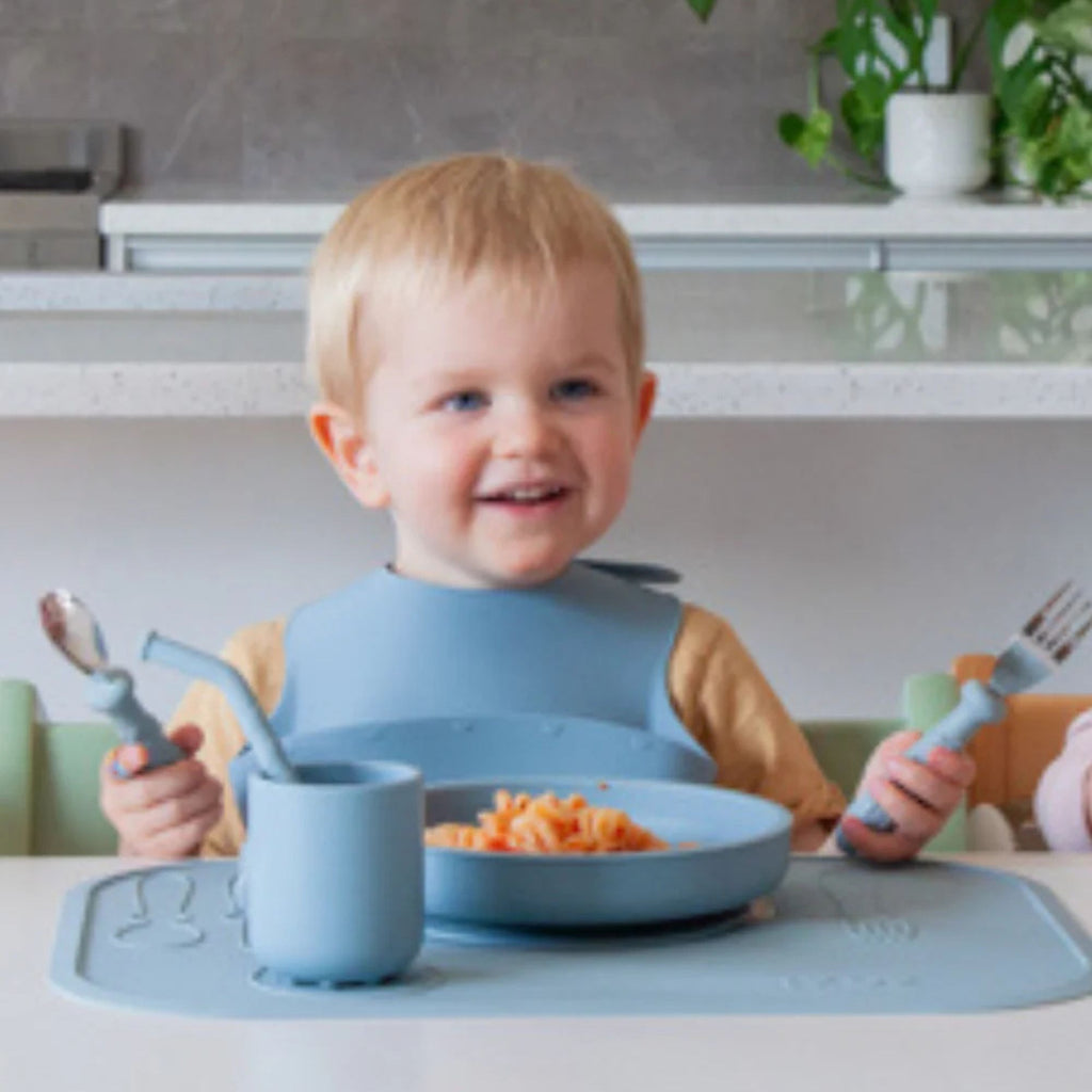 Child sitting at a table with blue dining set, smiling.