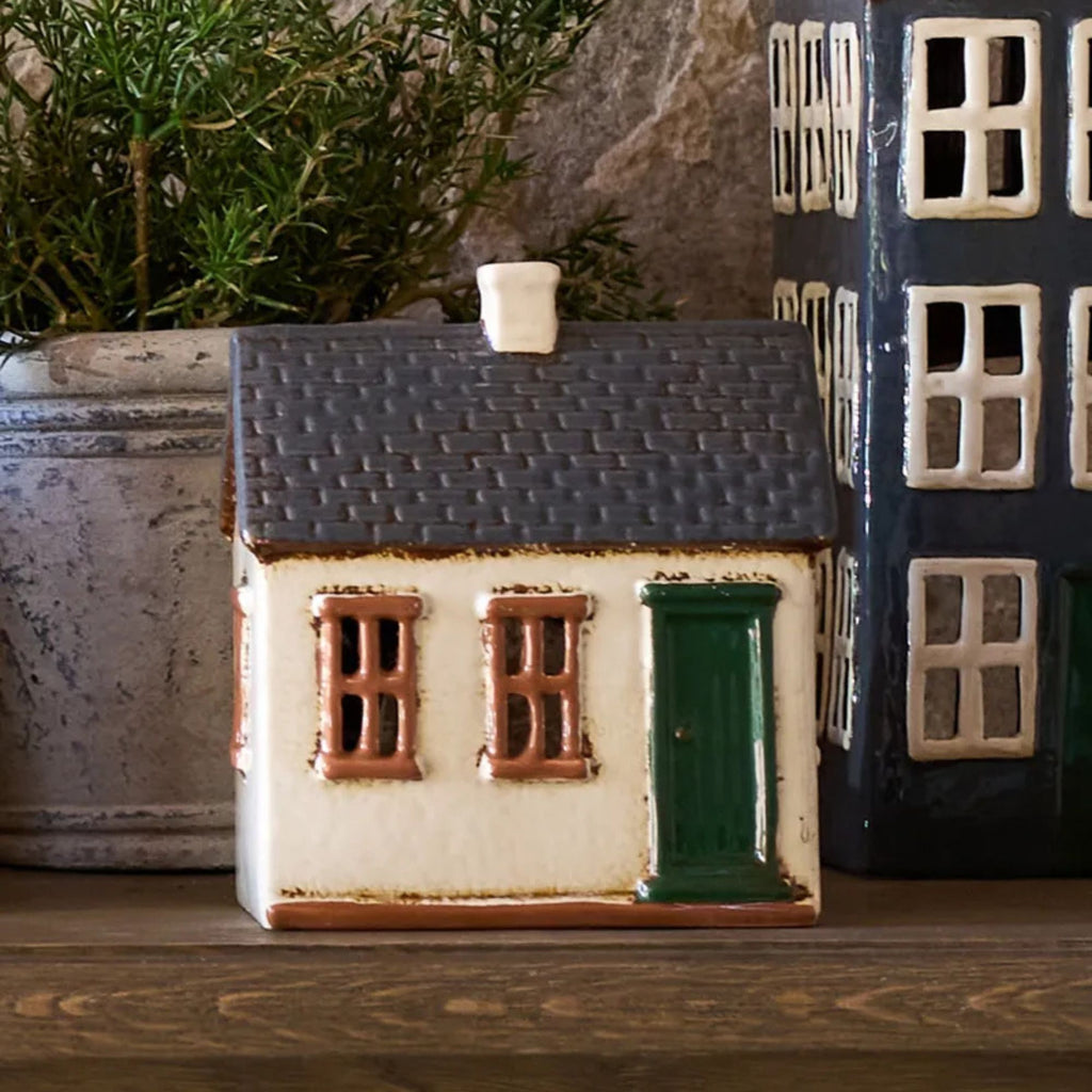 Small ceramic house model on a wooden surface with a plant in the background