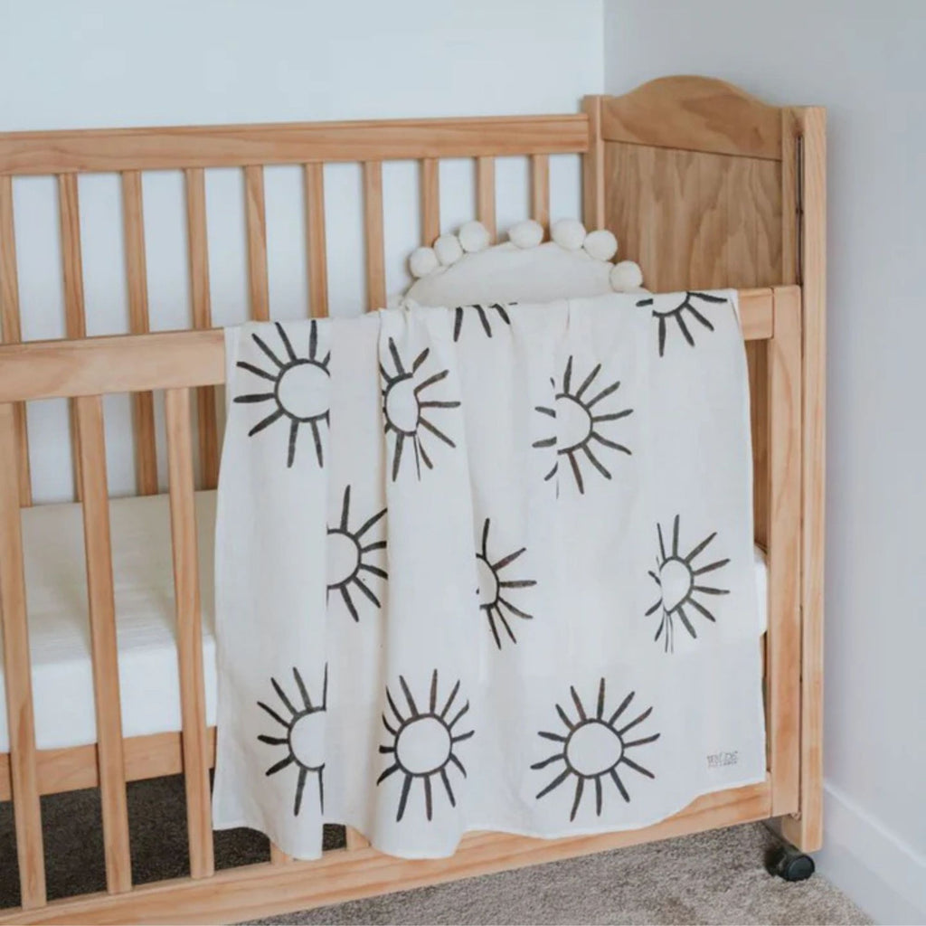 Wooden crib with a white blanket featuring black sun patterns