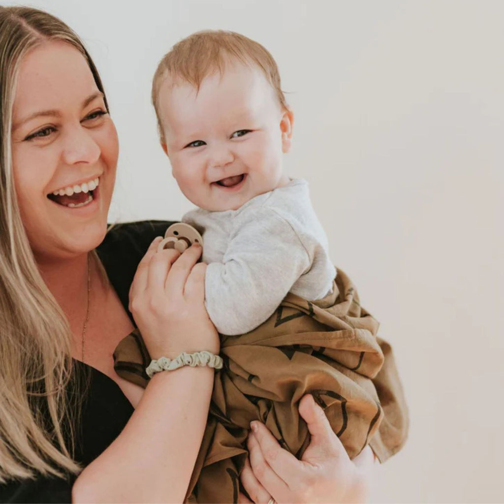 Woman holding a baby wrapped in a brown blanket against a plain background