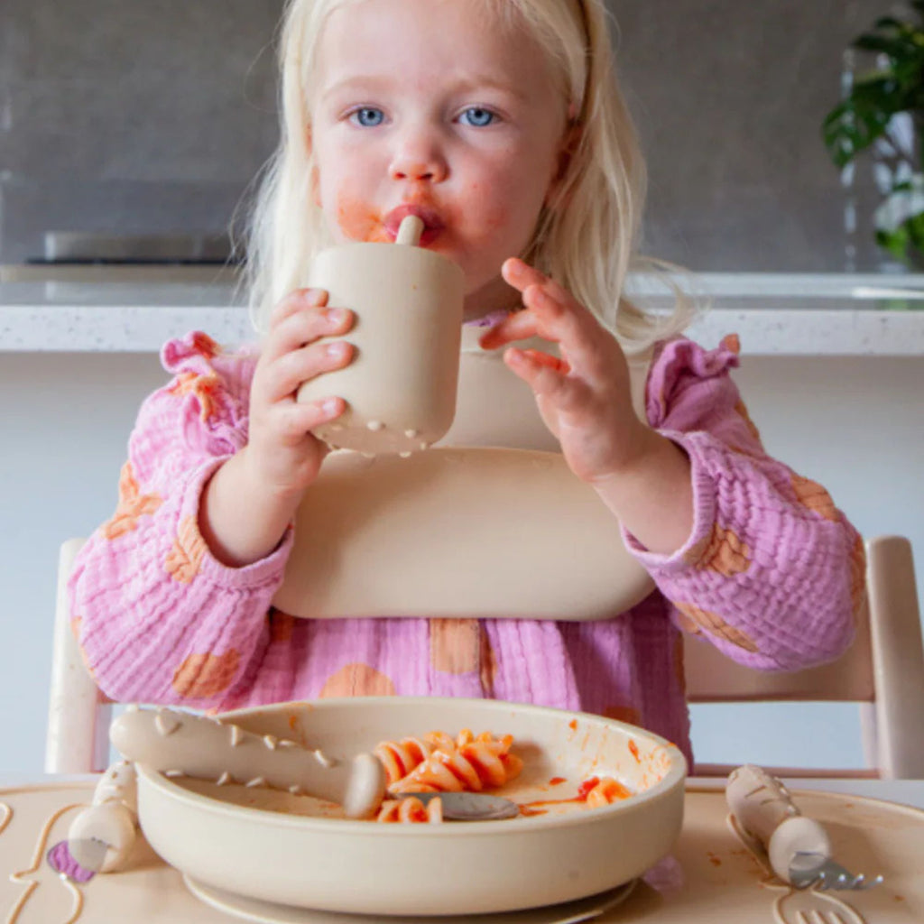 Child eating pasta with a high chair and bowl in a kitchen setting