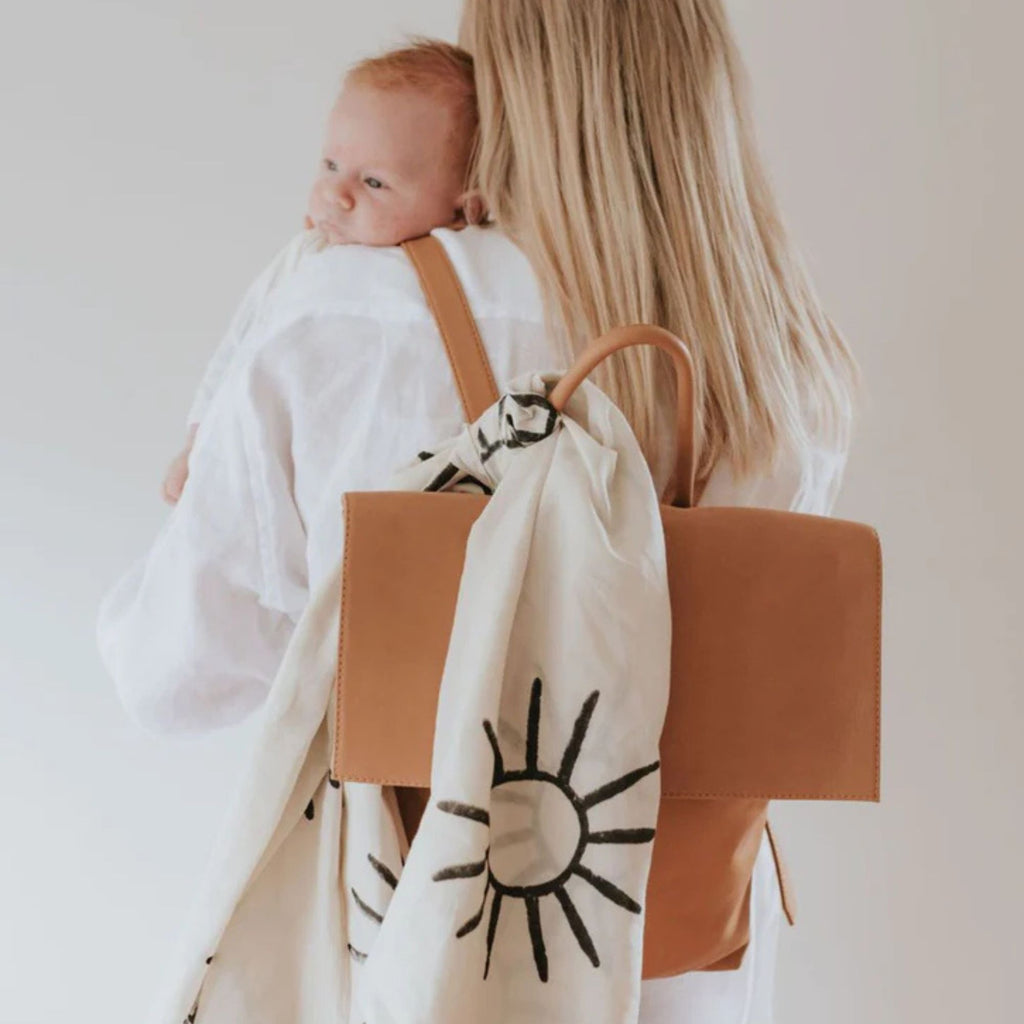Woman carrying a baby and a brown backpack with a sun design on a plain background