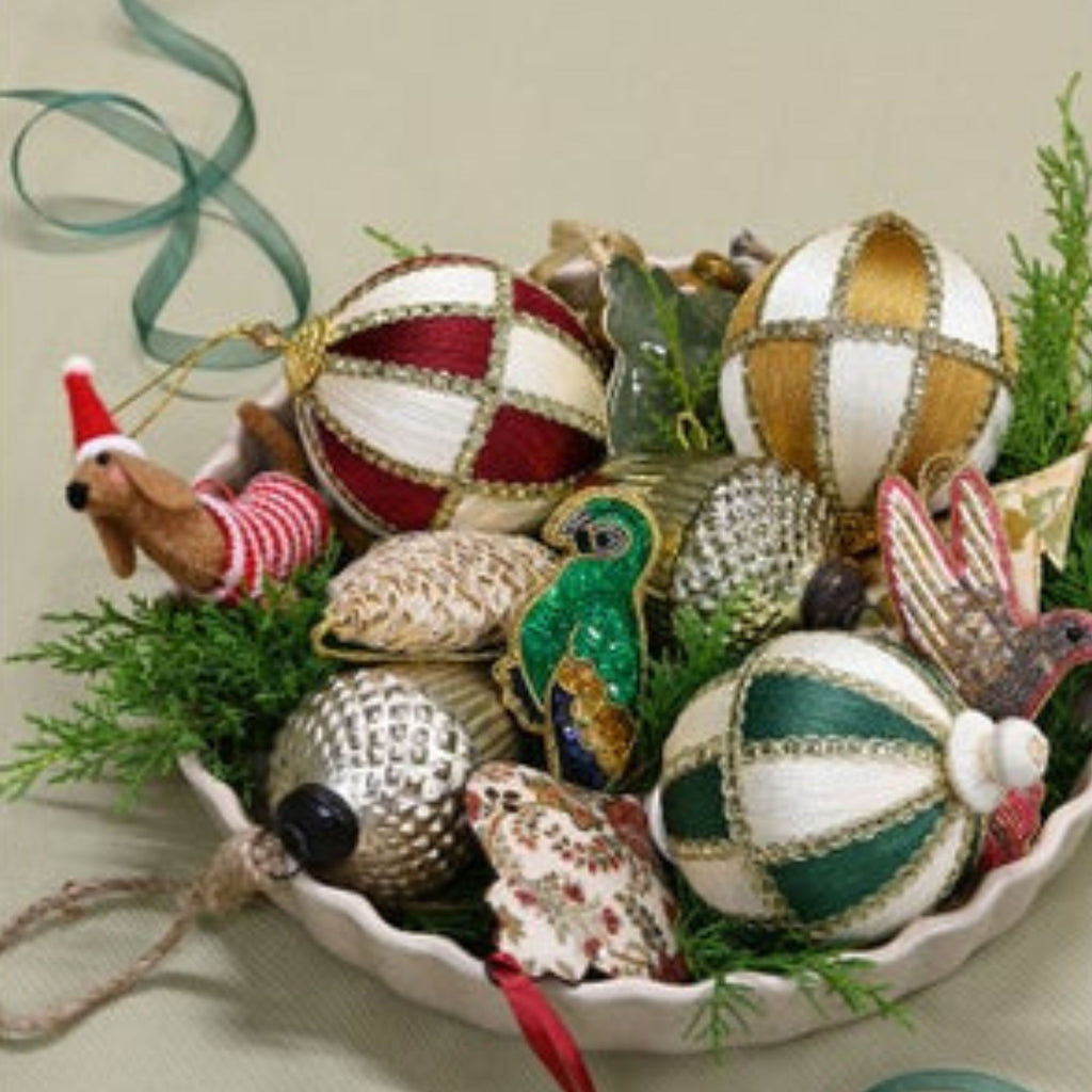 Decorative Christmas ornaments in a bowl with greenery on a neutral background