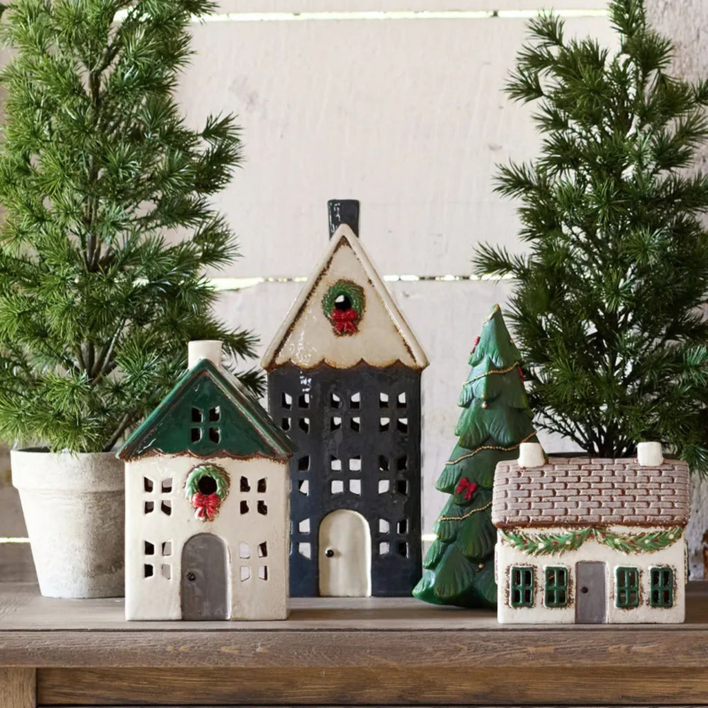 Decorative ceramic houses with Christmas trees and wreaths on a wooden surface.
