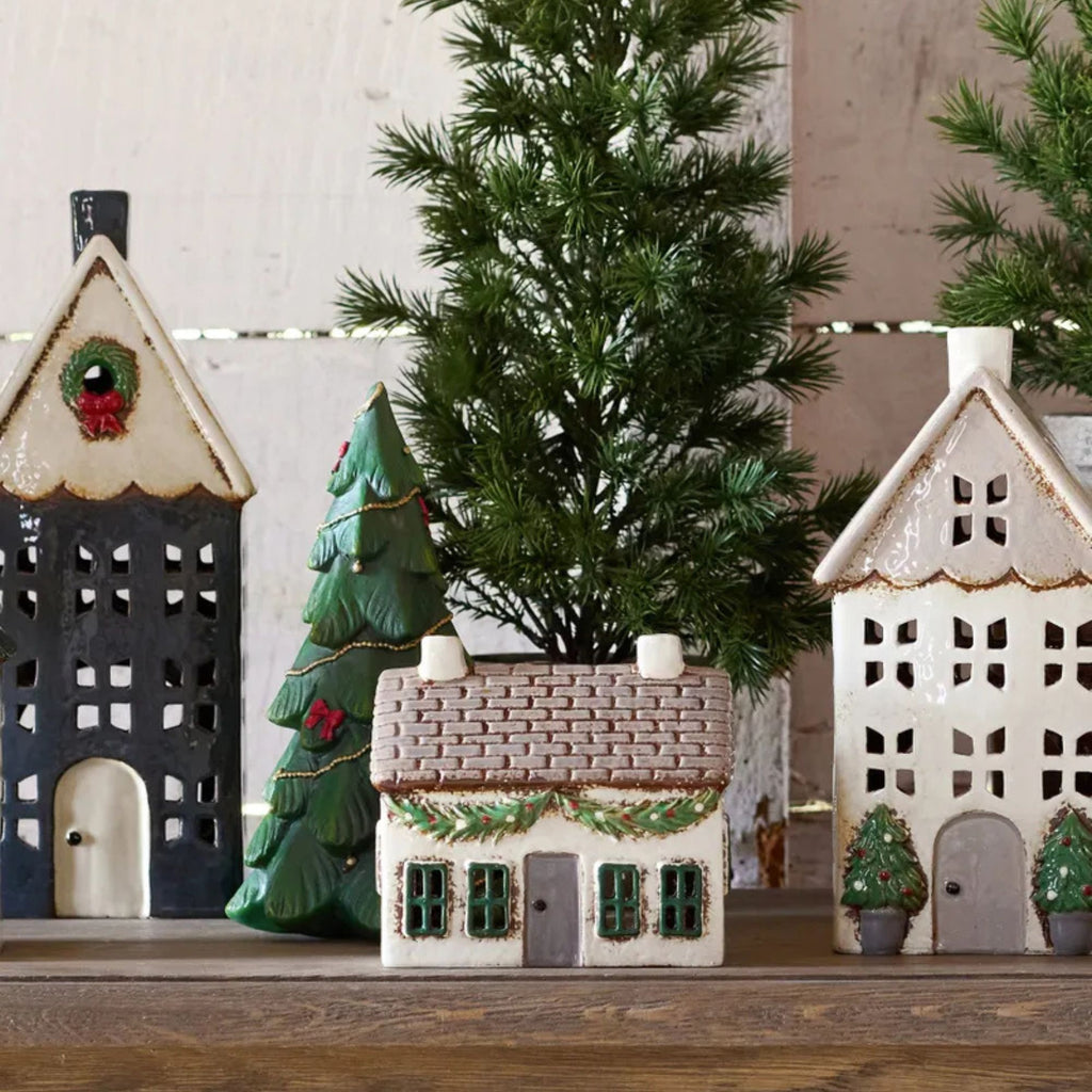 Decorative ceramic houses and a Christmas tree on a wooden surface with a white wall background.