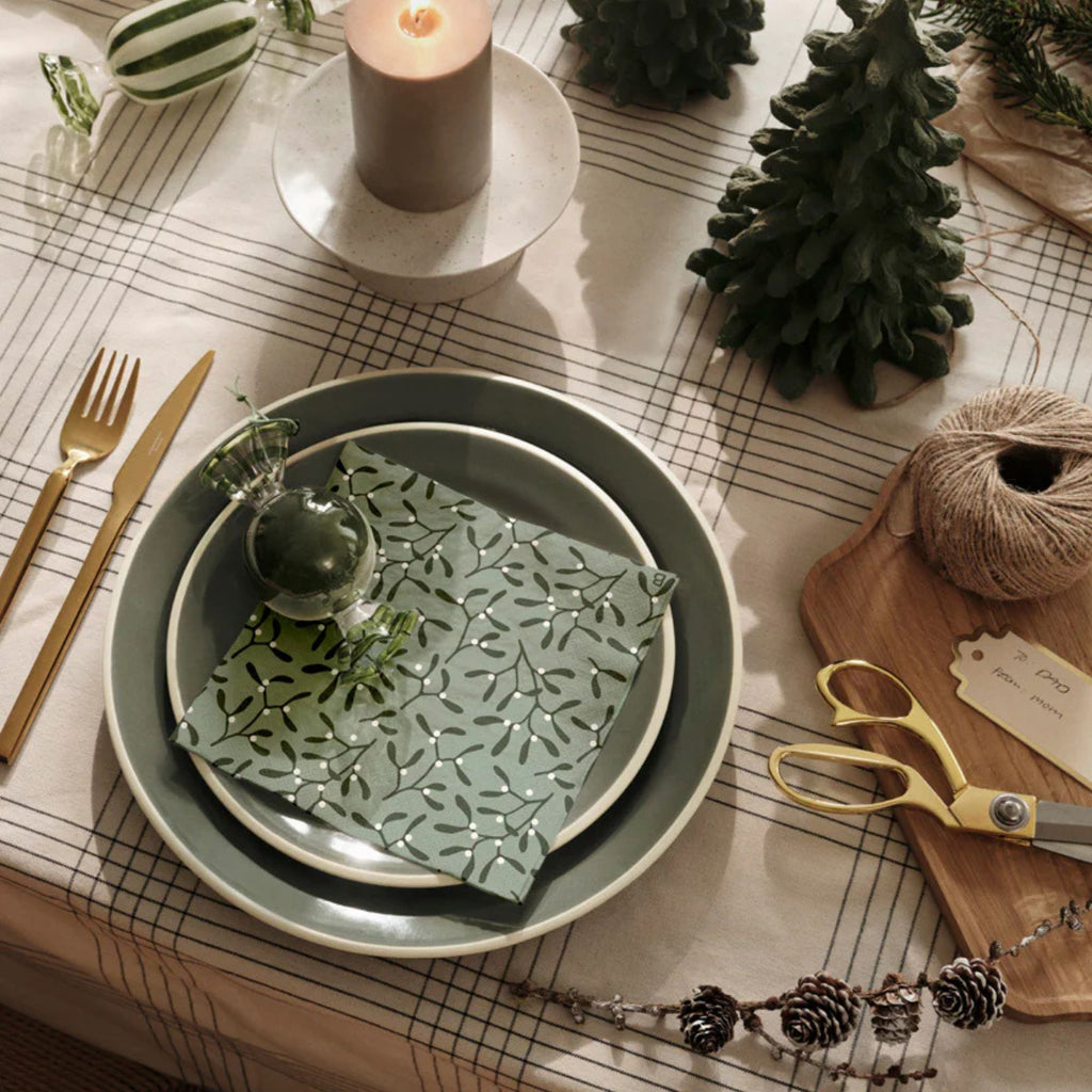 Decorative table setting with green ceramic dish, gold scissors, and candle on a checkered tablecloth.