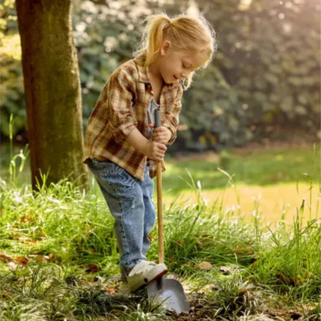 Child playing with a shovel in a grassy outdoor setting