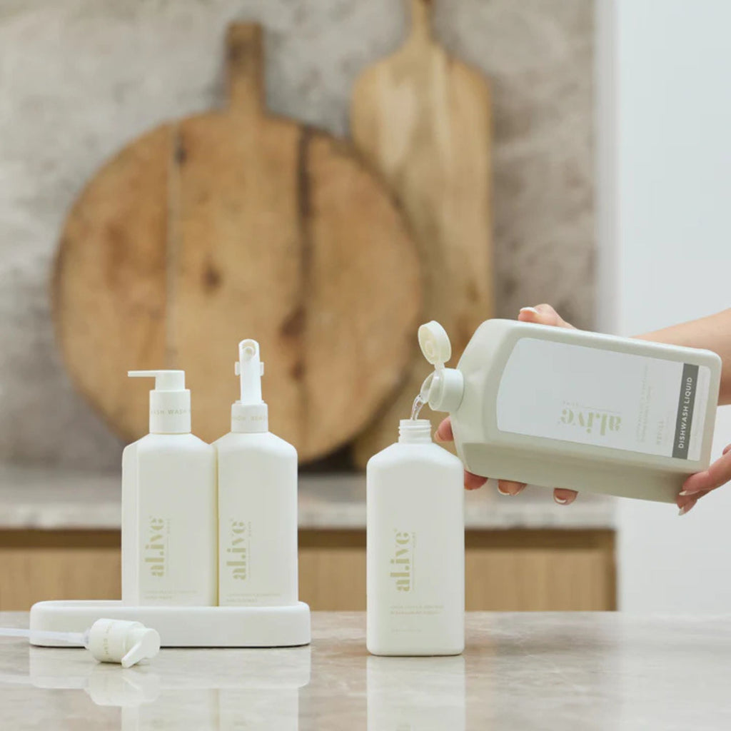 White bottles with 'alive' branding on a kitchen counter, with a person pouring liquid into one of the bottles.