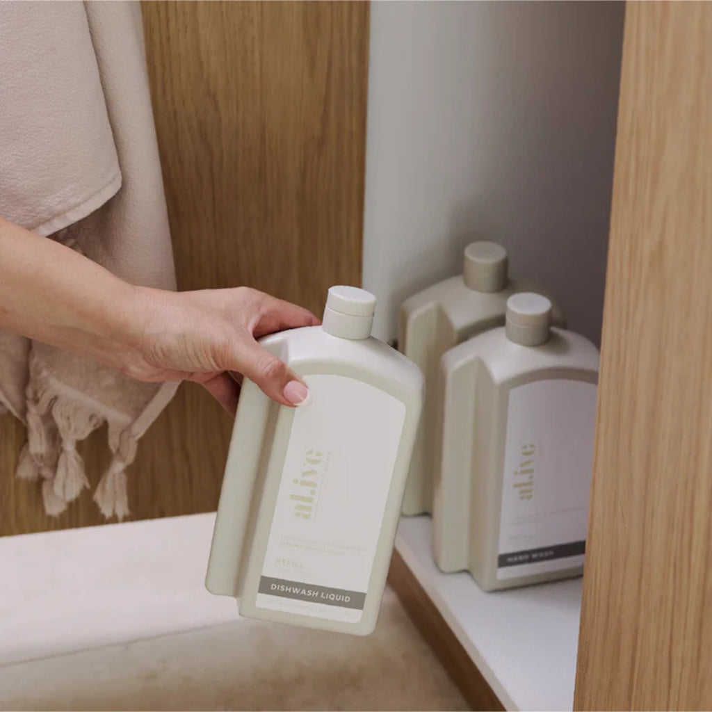Person holding a bottle of 'alive' skincare product in a bathroom setting