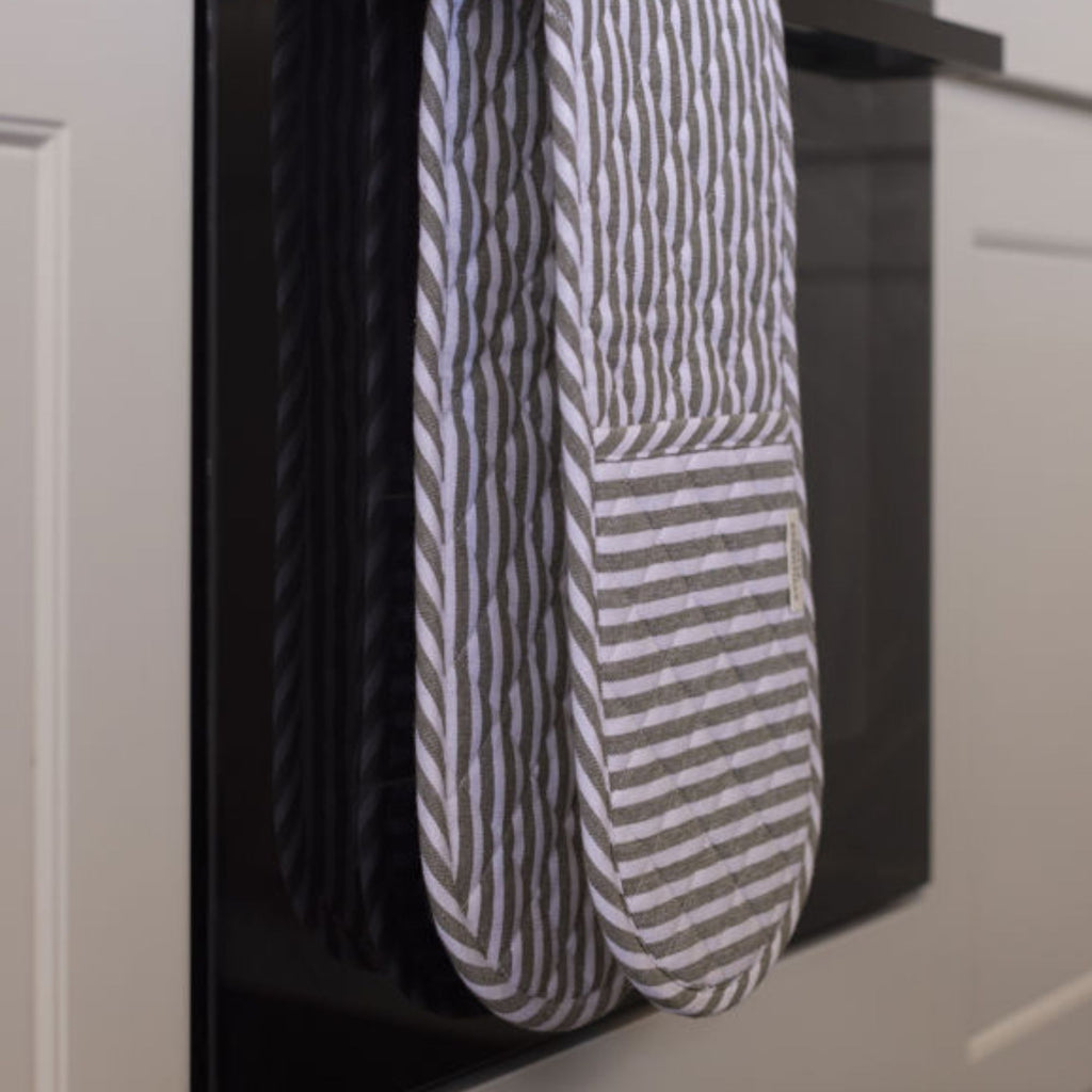 Striped oven mit hanging on a black rack against a neutral background