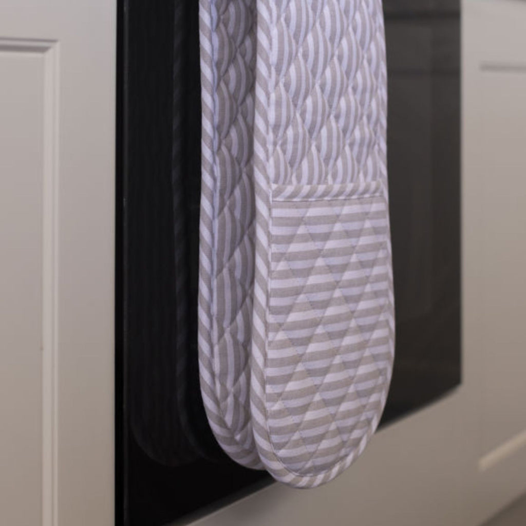 Pair of gray patterned oven mitts hanging on a black surface.