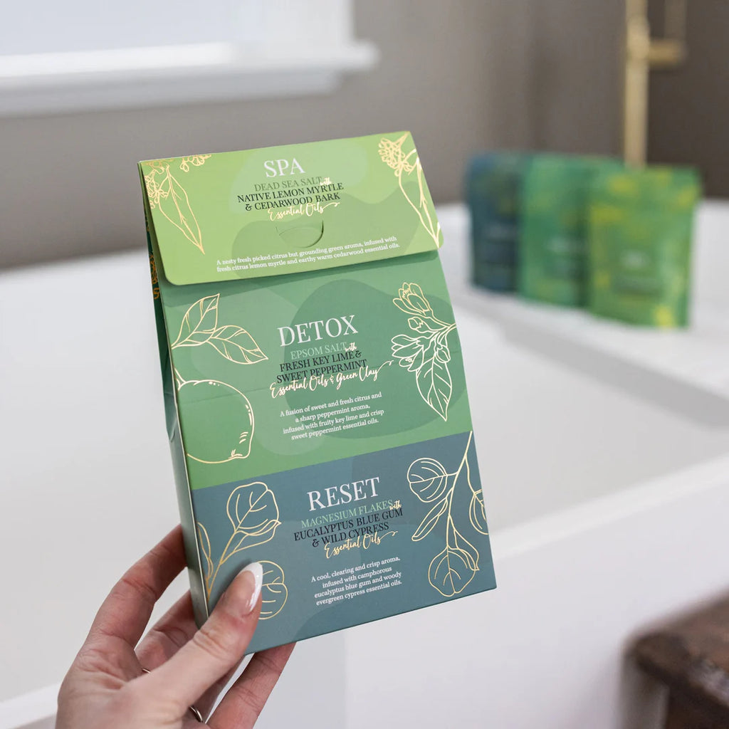 Hand holding a green and blue skincare product packaging with 'Detox' and 'Reset' text.