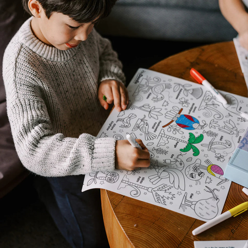 Child coloring a picture of a bird with markers on a coloring book.