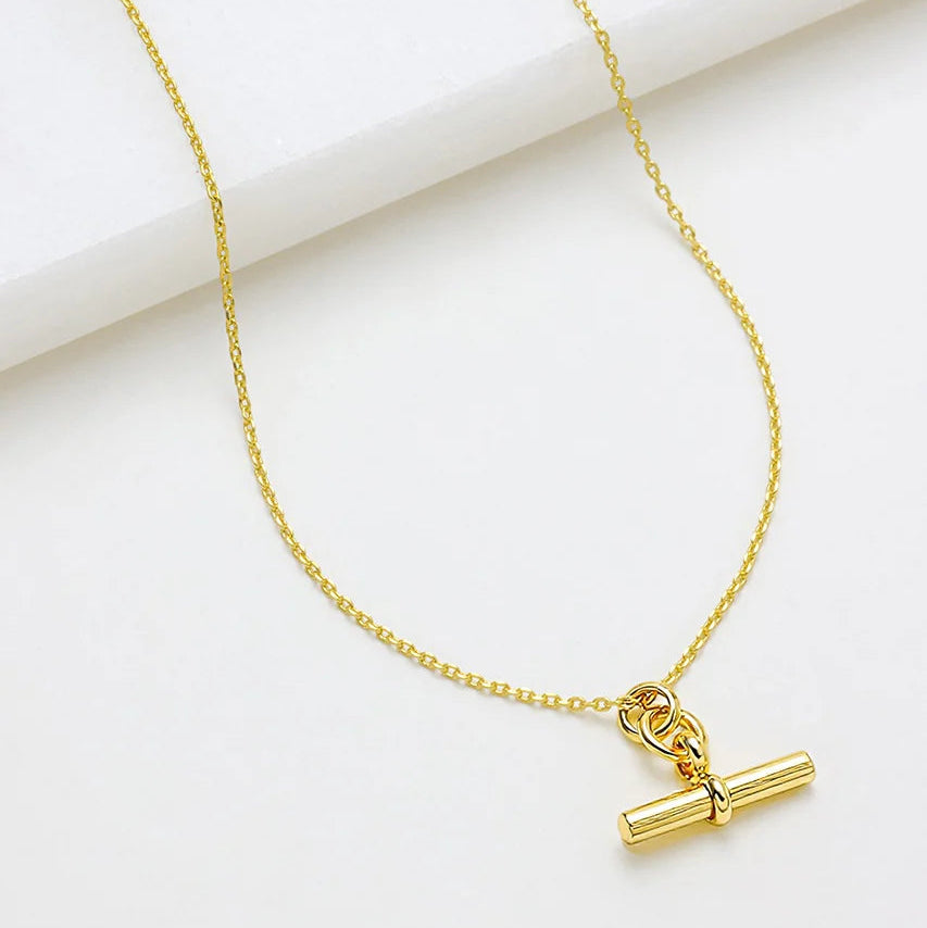 Gold necklace with a cylindrical pendant on a white background
