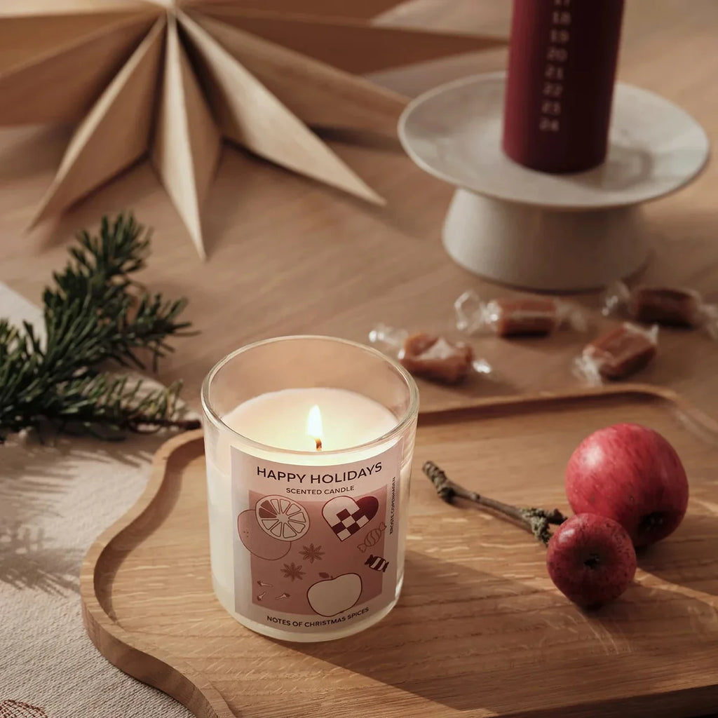Lit candle with 'Happy Holidays' label on a wooden surface with decorative elements