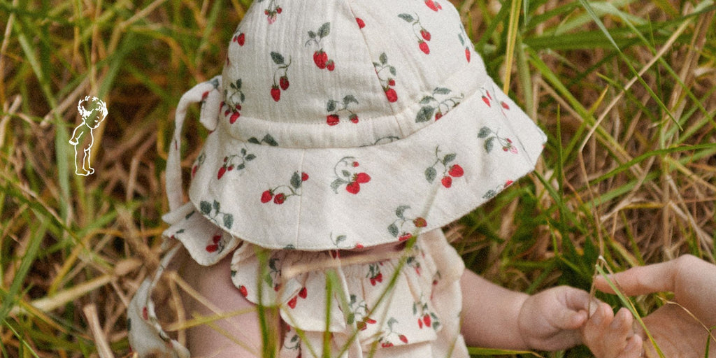 Baby in a floral hat and dress standing in grass