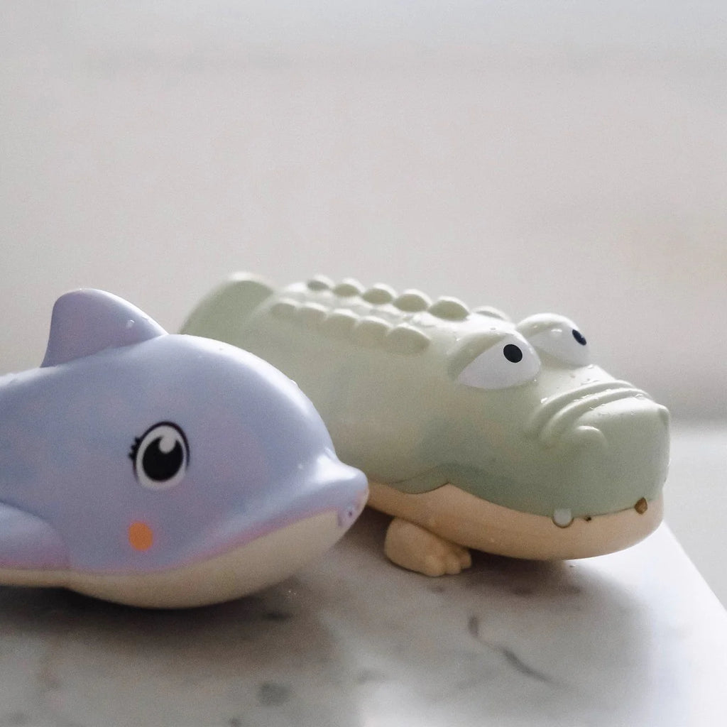 Toy dolphin and toy alligator on a light surface with a neutral background