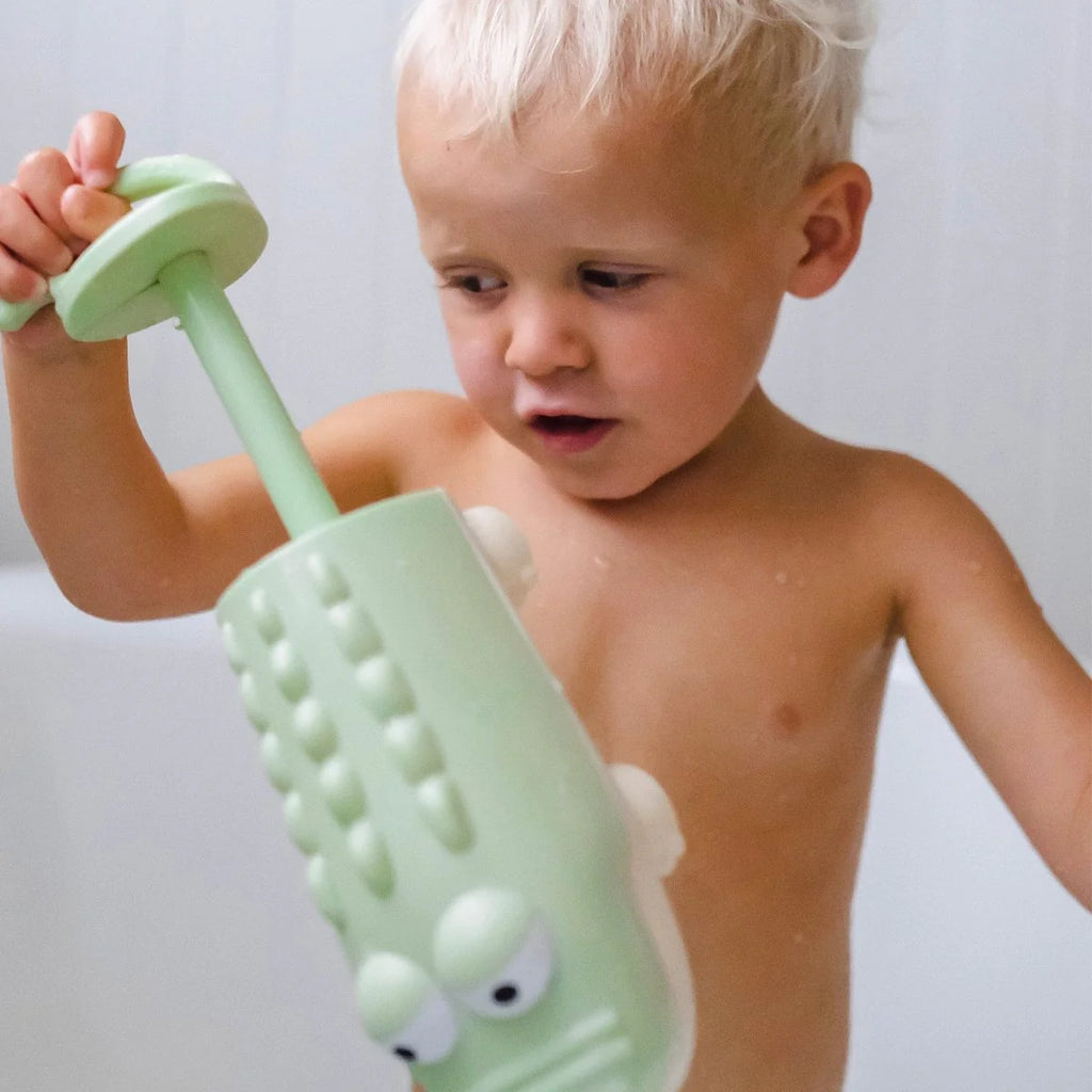 Child playing with a green textured toy in the bathtub