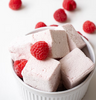 Pink marshmallows with raspberries in a white bowl on a light background
