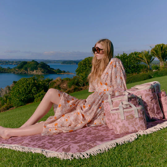 Woman sitting on a pink blanket with a scenic view of water and trees in the background