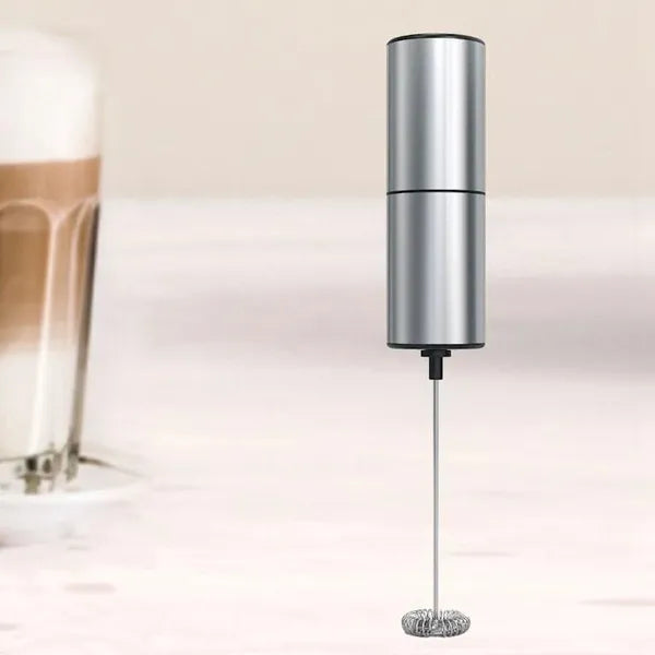 Metallic milk frother with a blurred background of a glass of coffee.