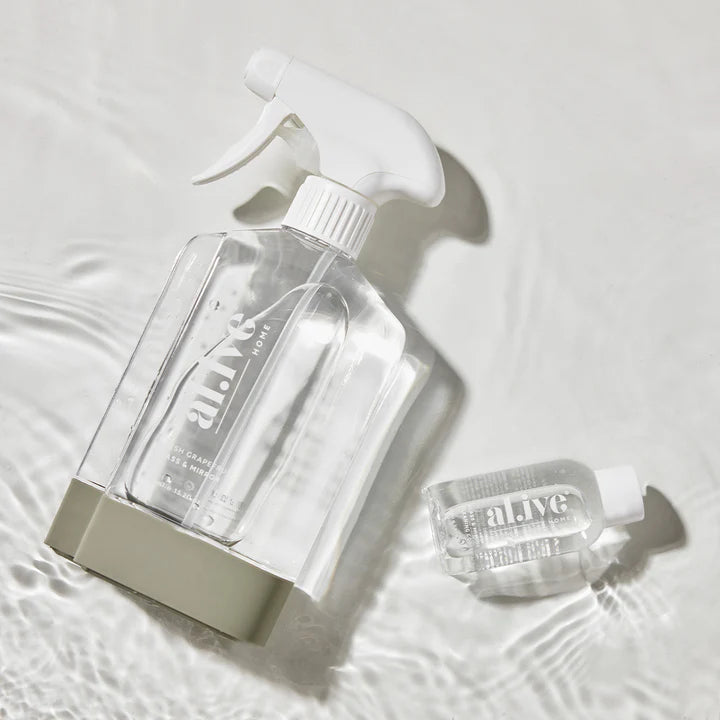 Clear spray bottle and small container with 'alive' branding on a light background