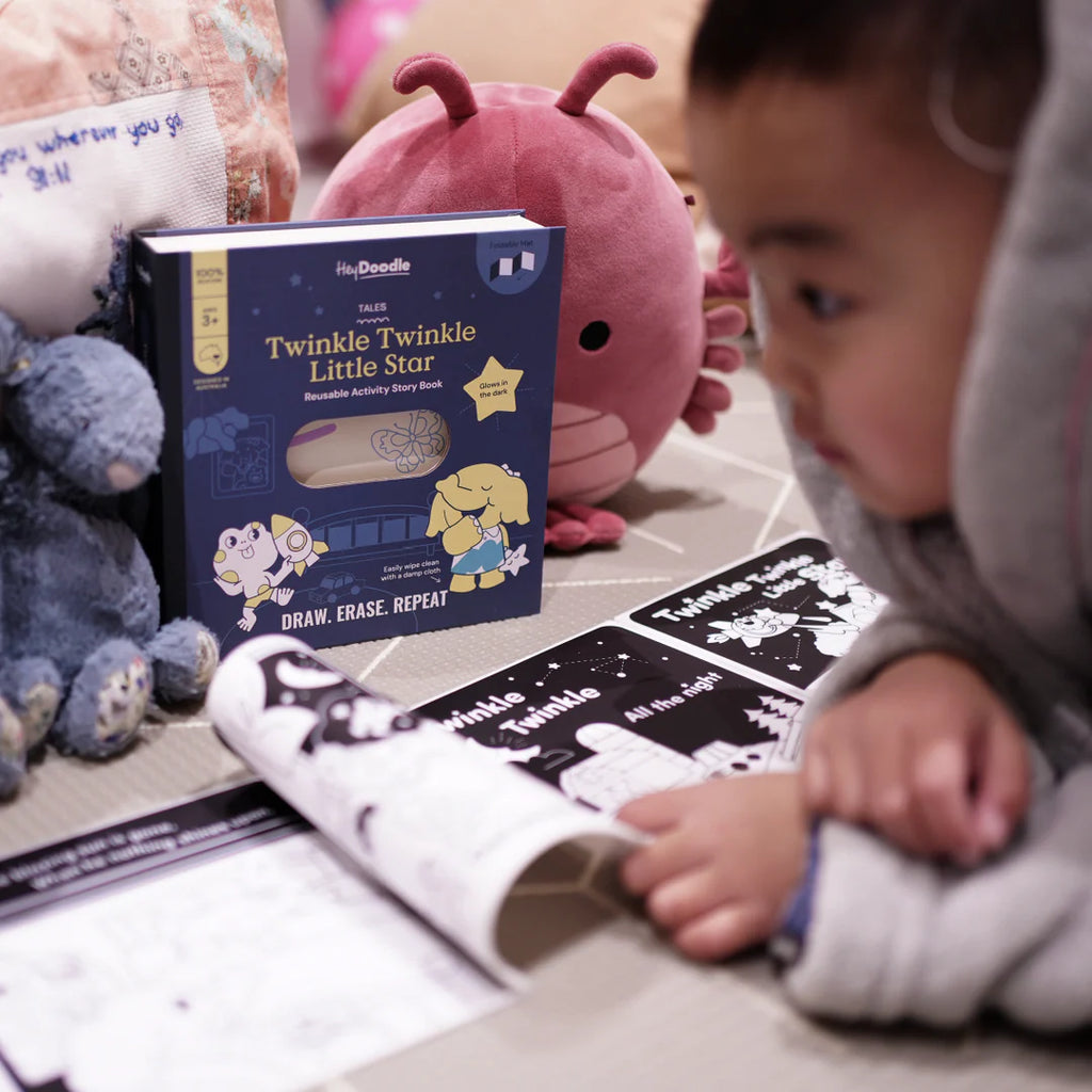Child interacting with educational materials including a book titled 'Twinkle Twinkle Little Star' and a reusable activity book.