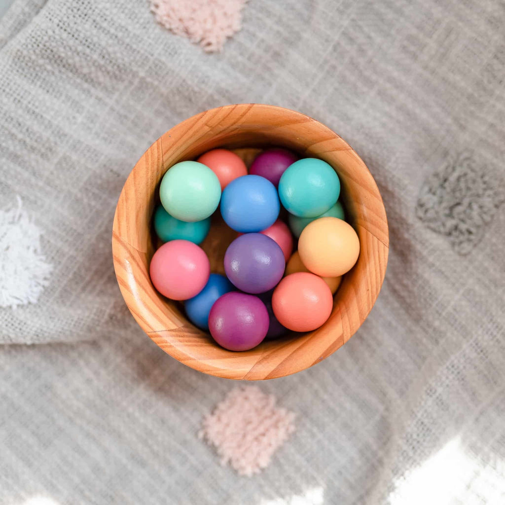 Wooden bowl filled with colorful round balls on a textured fabric background