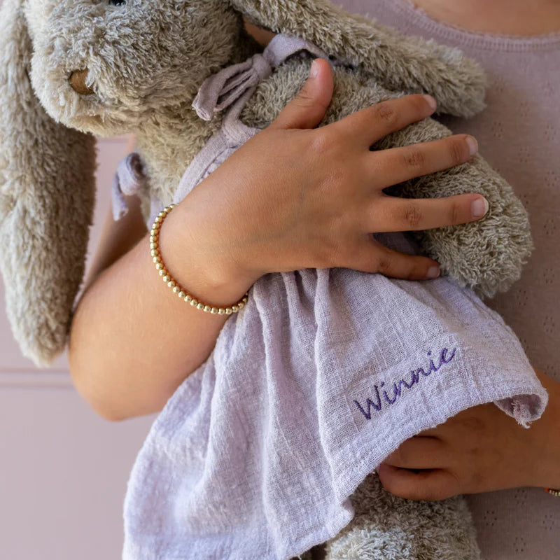 Child holding a plush bunny toy with a white blanket labeled 'Winnie' on a pink background